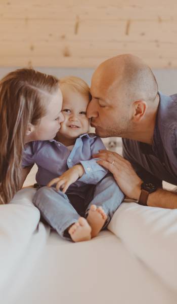 Eltern auf dem Bett kĂĽssen Kleinkind auf die Wange