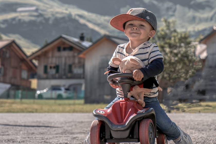 Junge mit Mütze und Kuscheltier auf Bobbycar im Malbun