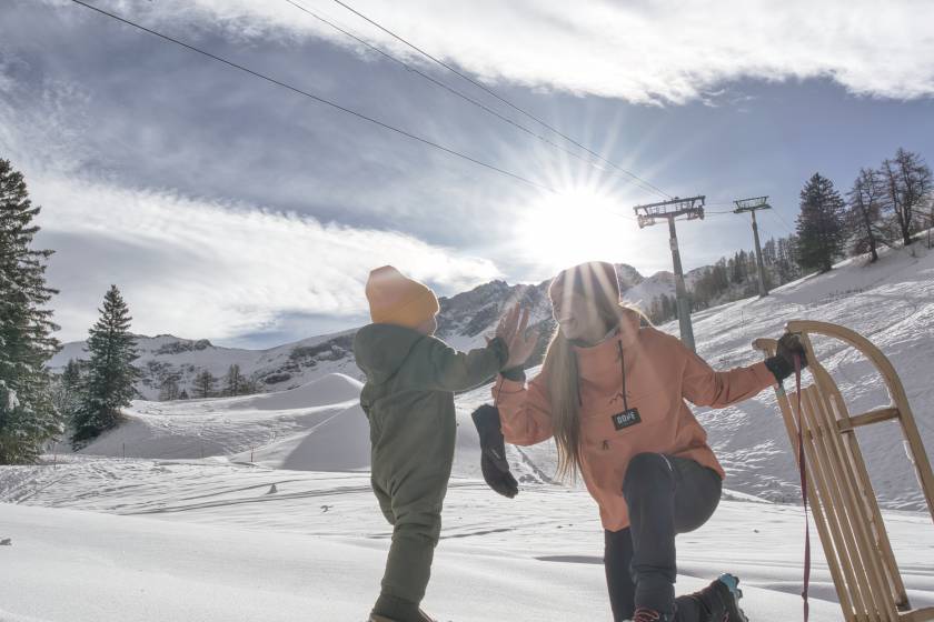 Mutter mit Schlitten und Kind bei Sonnenschein im Schnee