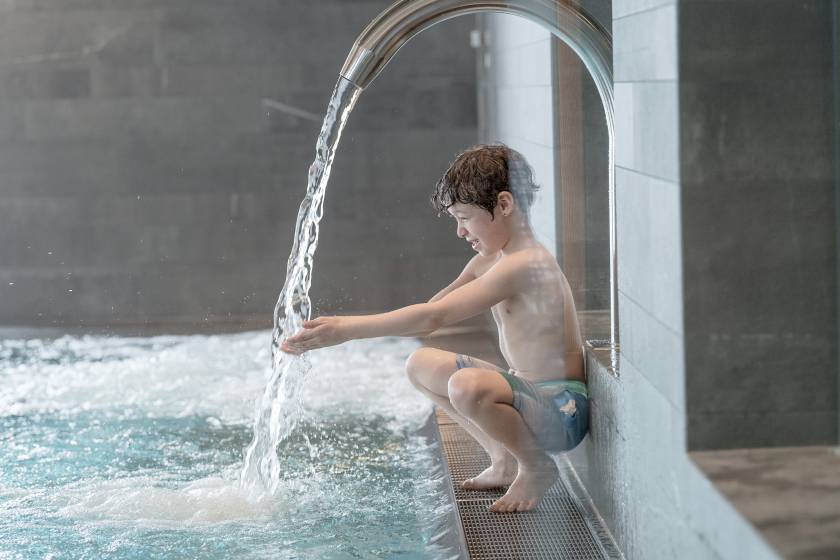 Kind am Pool-Wasserfall im Wellnessbereich des Familienhotel Gorfion Liechtenstein